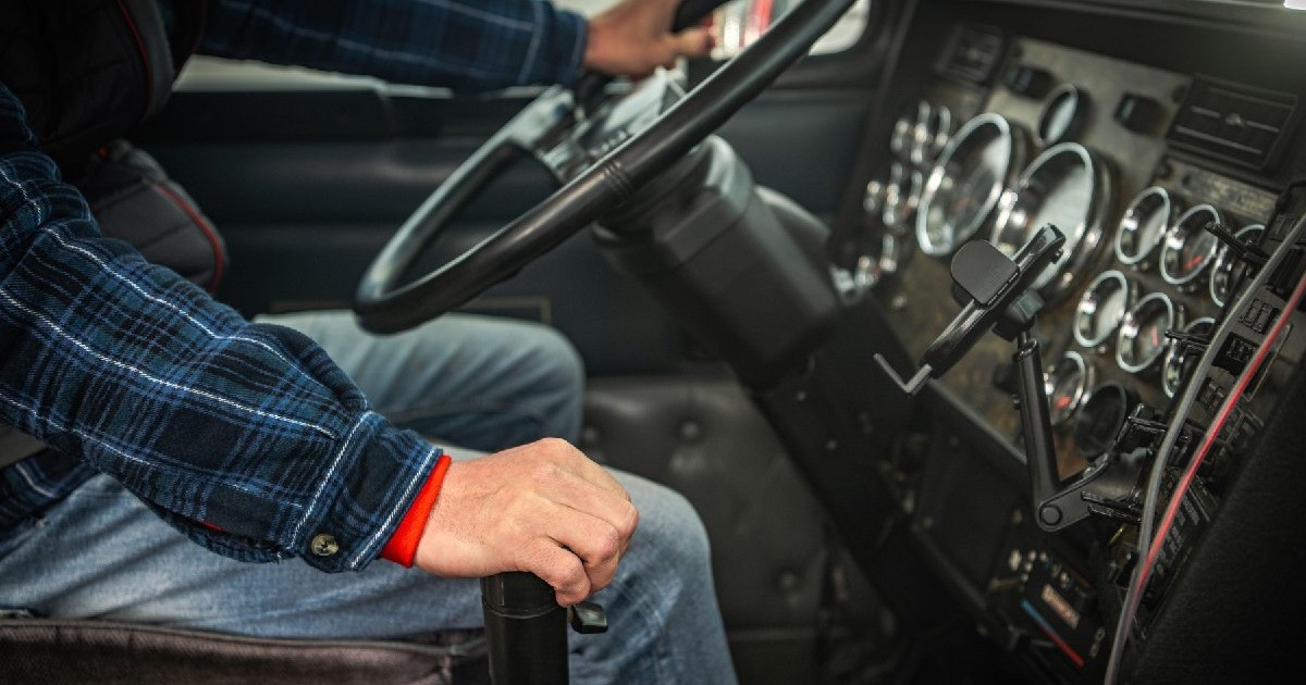 Un șofer ține volanul în timp ce schimbă vitezele în cabina unui camion mare. Atmosfera este concentrată și plină de activitate.