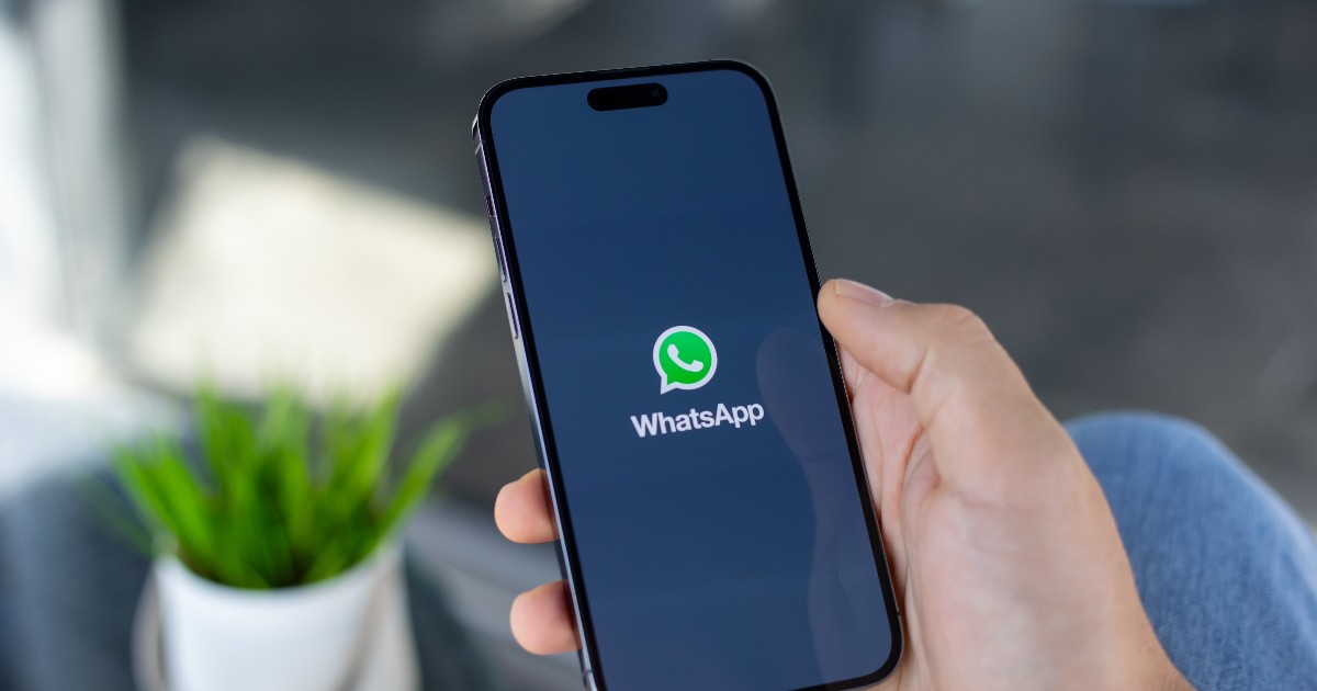 Imaginea arată o persoană care ține în mână un smartphone, pe al cărui ecran este deschisă aplicația WhatsApp. Telefonul are un design modern, cu margini subțiri și un ecran mare, iar logo-ul aplicației este vizibil clar pe fundal închis.