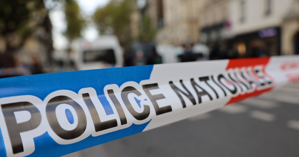 O zonă de pe stradă unde a avut loc o crimă a fost delimitată de poliție și nu se mai trece, iar pe un fundal neclar se vede o mașină de poliție