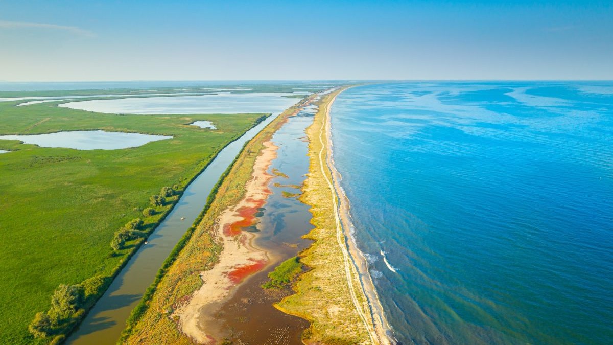 Malul Mării Negre în Delta Dunării. Vedere aeriană asupra minunatului sat Gura Portitei din România, într-o frumoasă zi însorită. Peisaj cu apa albastră a mării și alge roșii