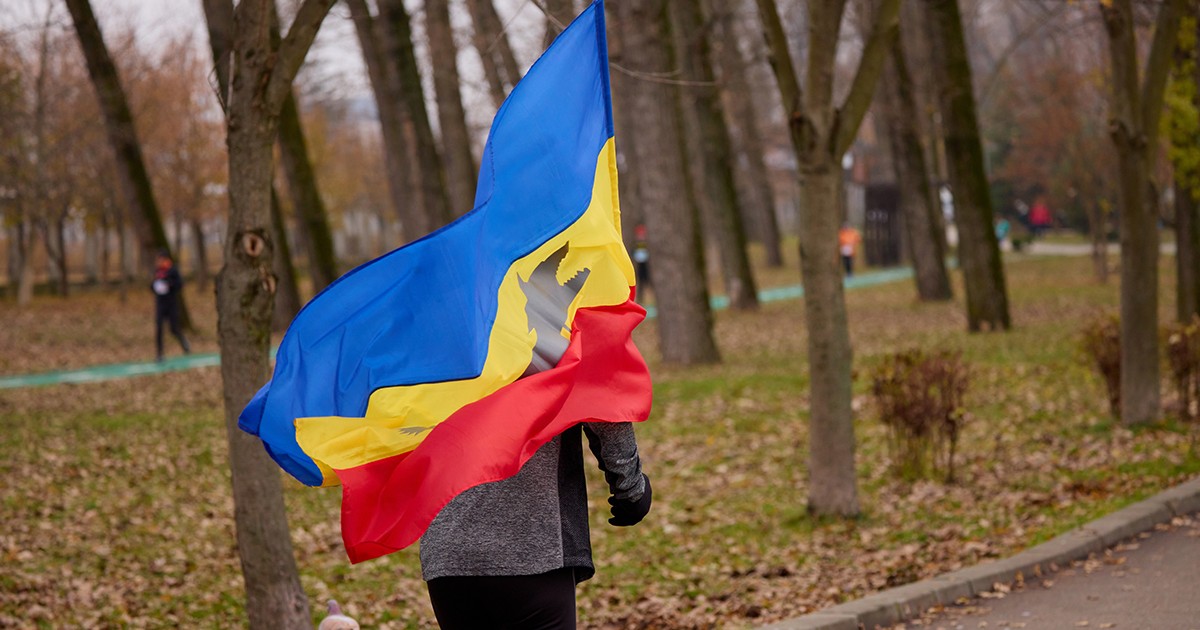 Un barbat alearga in parc infasurat intr-un steag tricolor