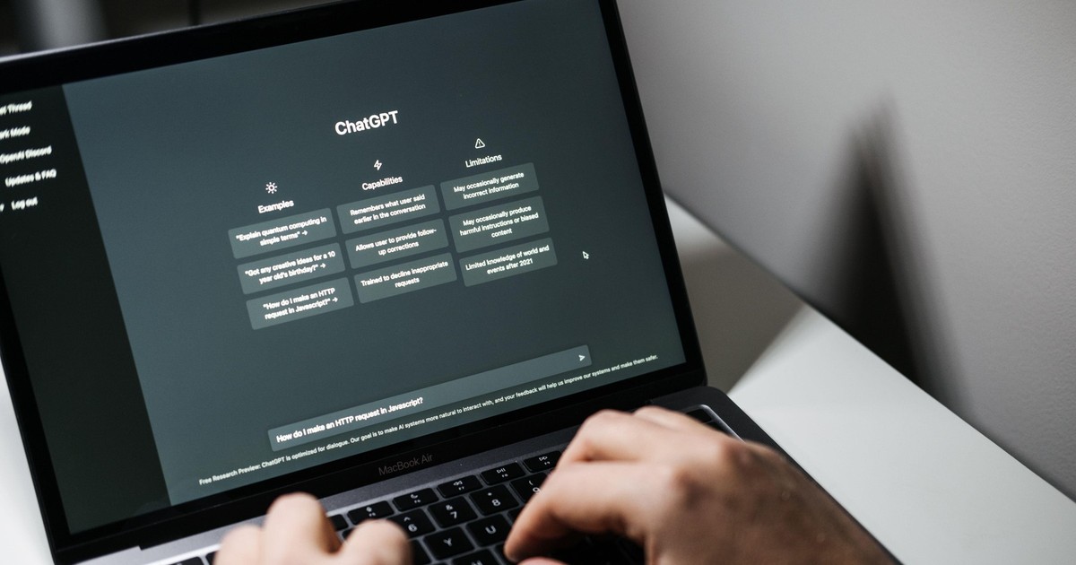 Imagine cu un laptop și cu mâinile unui bărbat pe tastatură. Pe ecranul dispozitivului este afișată aplicația ChatGPT