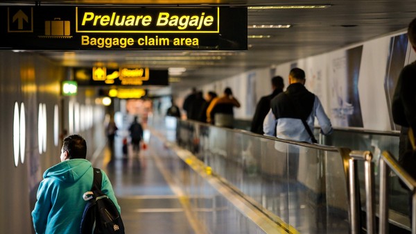 Imaginea surprinde culoarul de acces către zona de preluare a bagajelor dintr-un aeroport, semnalizată printr-un panou luminos cu inscripția „Preluare Bagaje / Baggage claim area”. Foto: Shutterstock