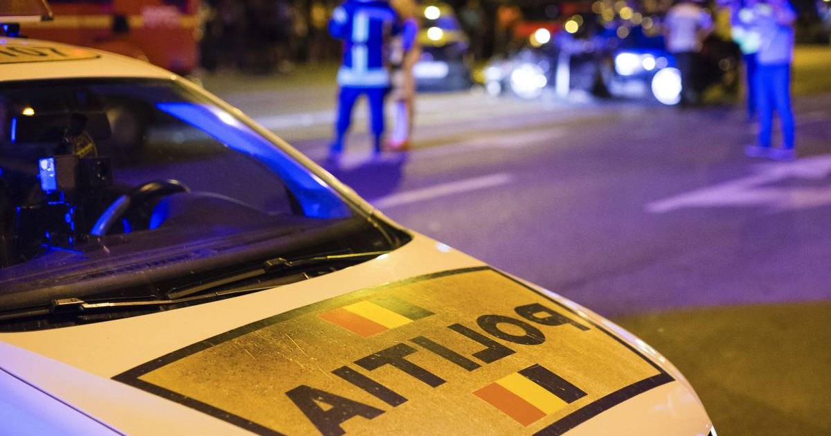 Fotografie în care în prim plan este o mașină a poliției, pe fundal agenți de poliție care fac măsurători în urma unui accident auto.