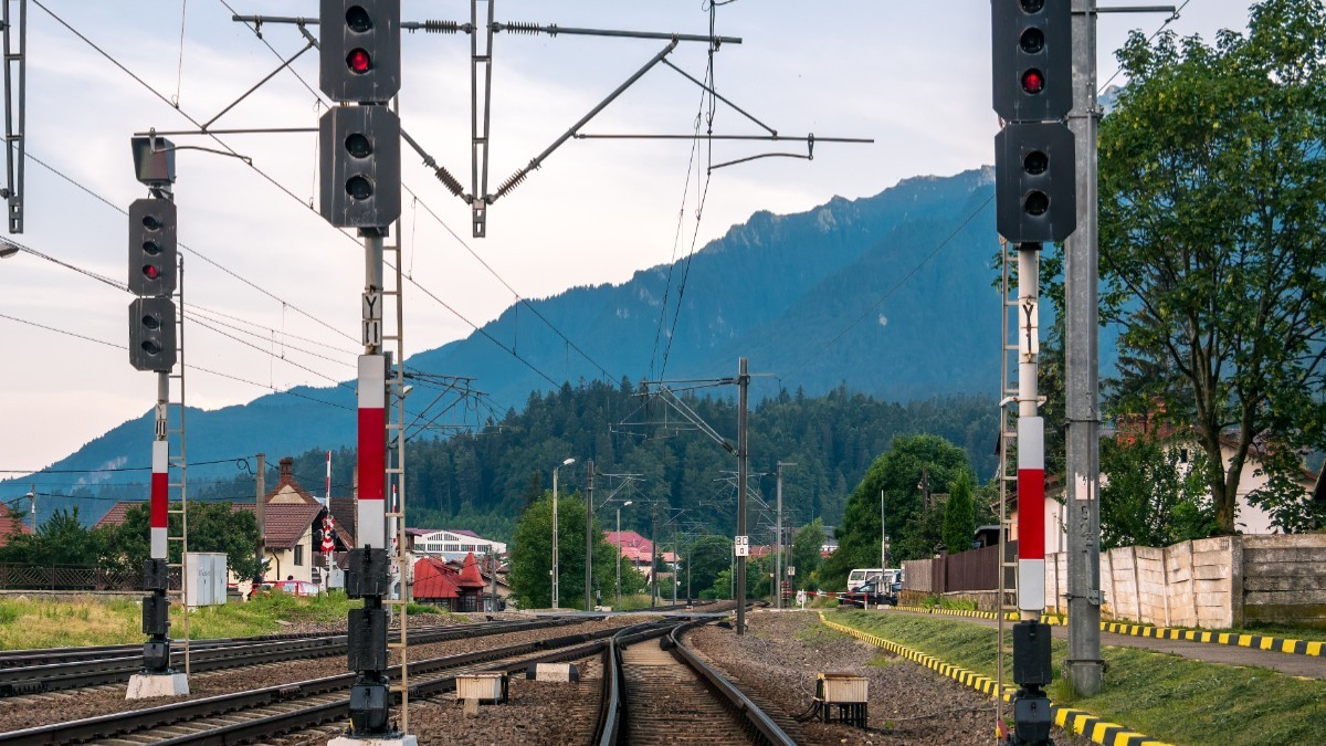 Trei linii de cale ferată într-o gară dintr-o zonă montană din România, luminile roșii de semnalizare sunt aprinse