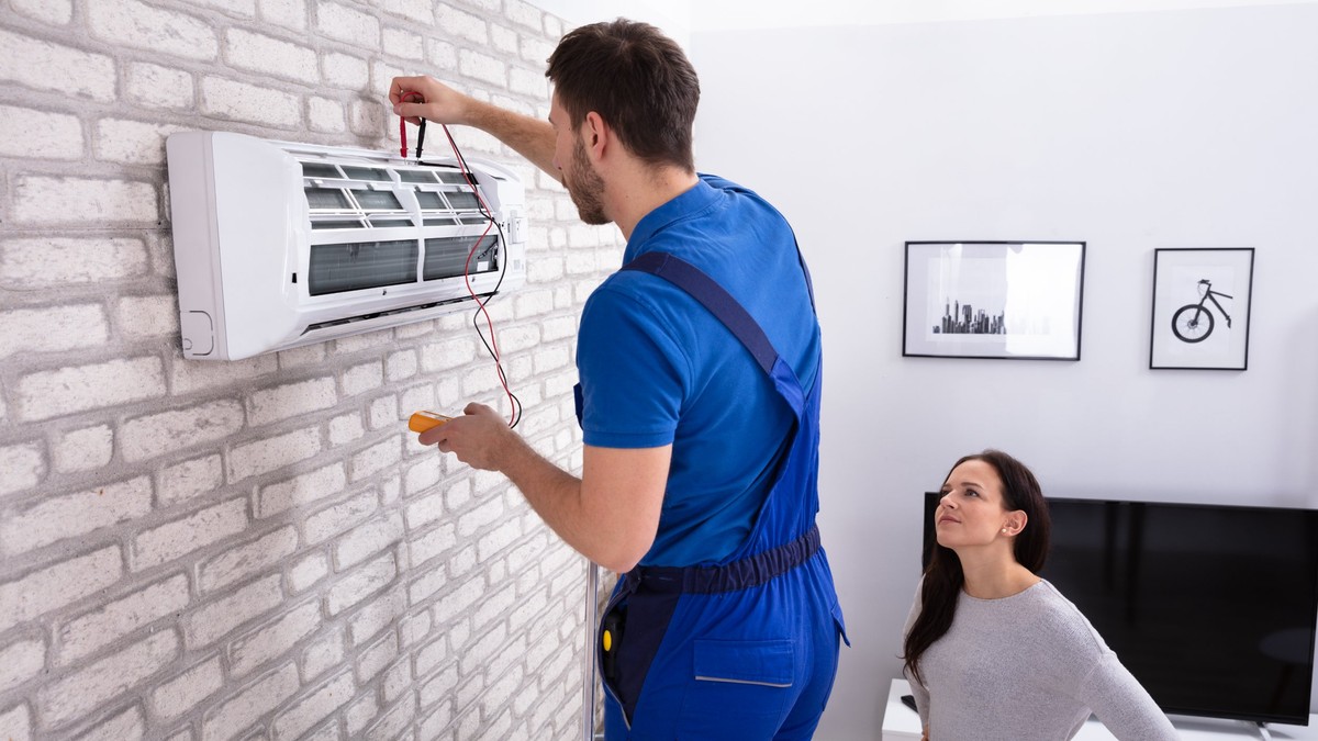 Top 10 cele mai bune aparate de aer condiționat sub 1.500 de lei - O femeie priveşte cum un tehnician testează o unitate internă a unui aparat de aer condiţionat