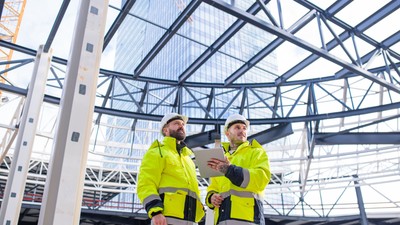 Men engineers standing outdoors on construction site, using tablet.