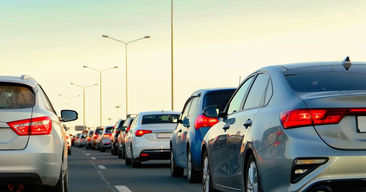 Mai multe mașini aflate în linie, pe un drum cu două benzi pe sens, posibil o autostradă.