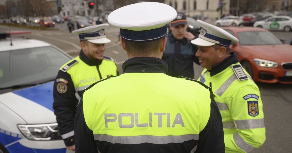 Trei polițiști, îmbrăcați în uniformă, în timp ce discută lângă o autospecială de Poliție, pe o stradă din București