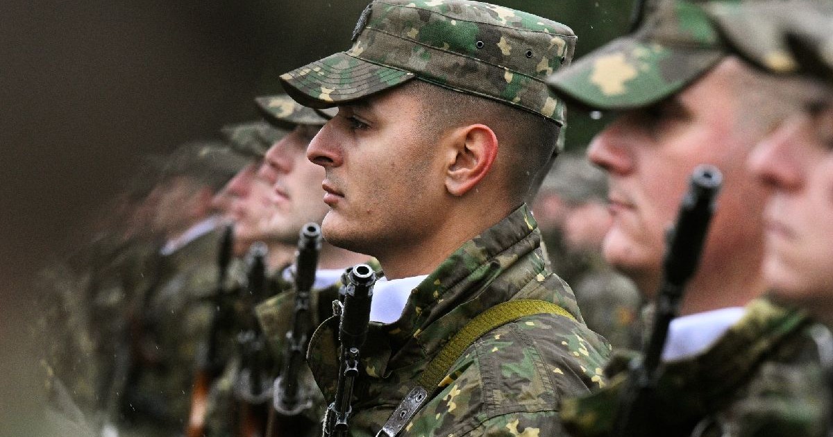 Fotografie cu un grup de soldați în uniforme de camuflaj, stând în linie, în aer liber.