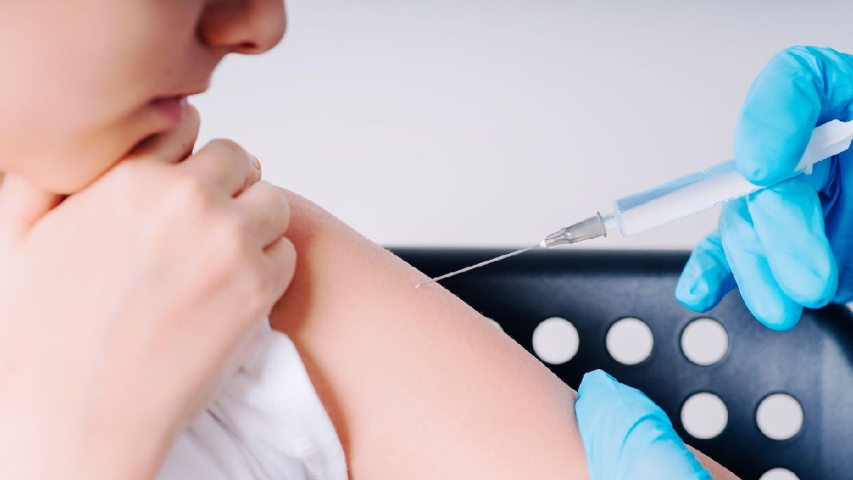 Un copil este vaccinat în mână de un cadru medical care poartă mănuși de plastic albastre