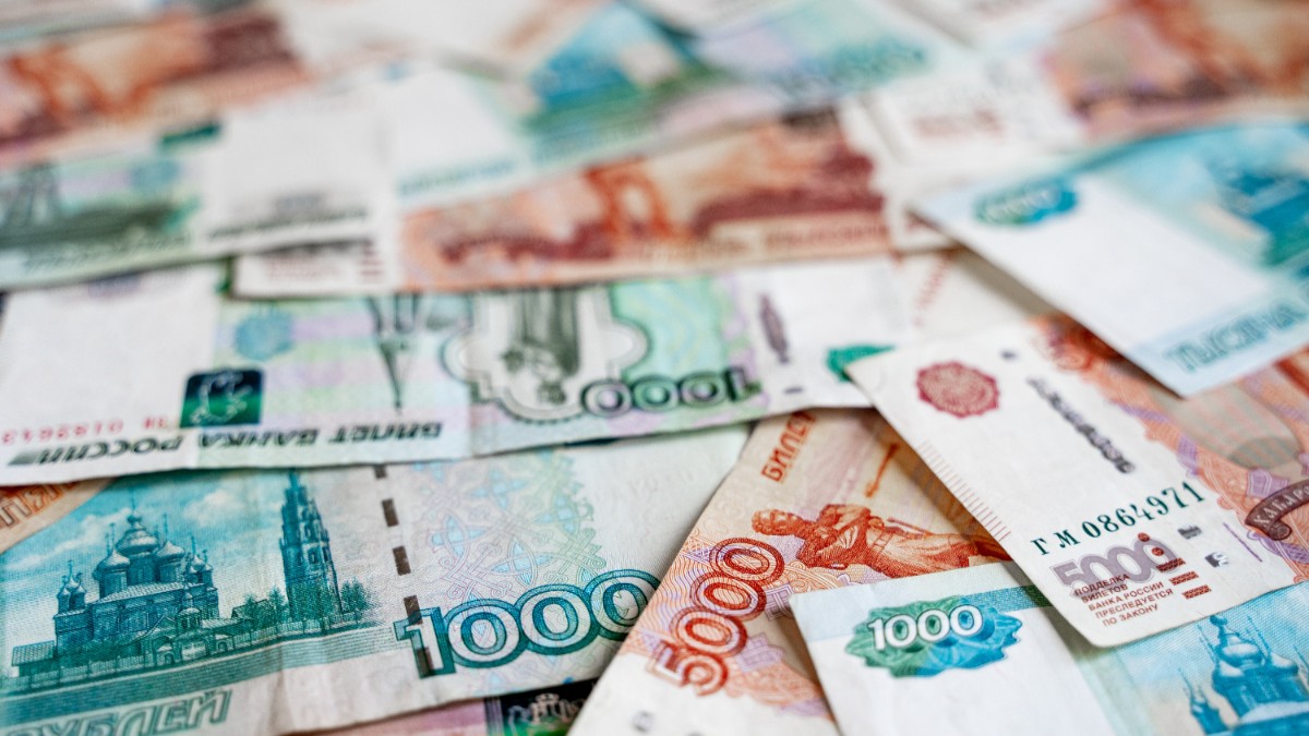 Bancnote de ruble rusesti, de culoare portocaliu, albastru și verde, de diferite valori, împrăștiate pe o suprafață