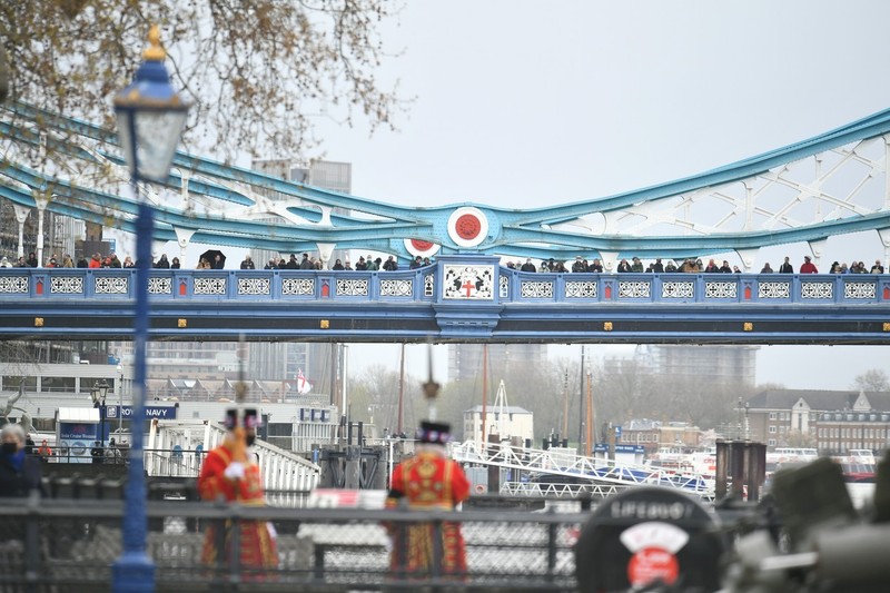 Sute de oameni se află aliniați pe Tower Bridge din Londra și privesc salvele de tun trase în onoarea prințului Philip, decedat ieri, la 99 de ani. Foto: Profimedia
