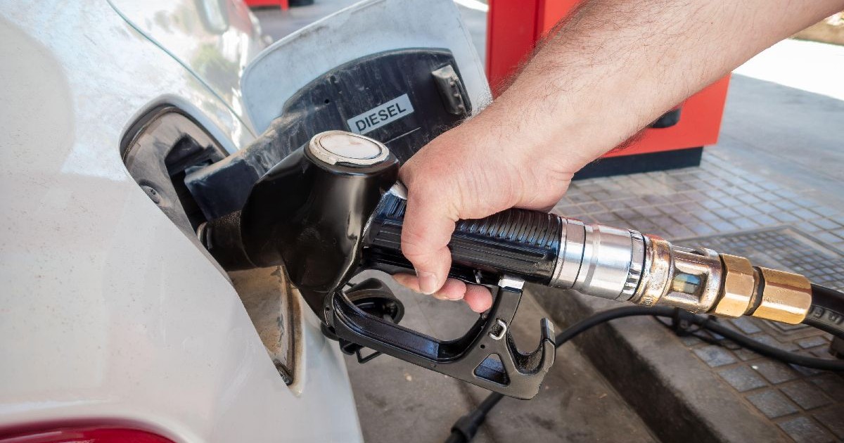 O persoană alimentează carburant cu pistolul introdus în fanta de la rezervorul unei mașini albe, într-o benzinărie
