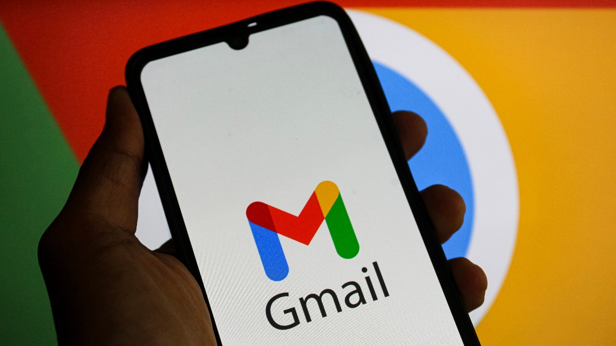 Imaginea prezintă un smartphone ținut în mână, pe al cărui ecran este afișată sigla serviciului de email Gmail (litera "M" stilizată în culorile roșu, albastru, verde și galben) împreună cu numele. Pe fundalul estompat se pot distinge culorile vii și elementele grafice specifice altor produse Google, subliniind asocierea aplicației cu ecosistemul companiei.