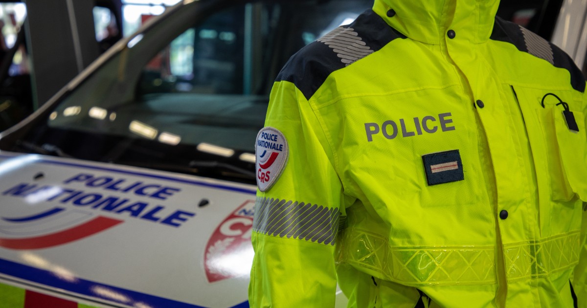 Un polițist din Franța care stă lângă mașina de intervenție și poartă o geacă verde-neon