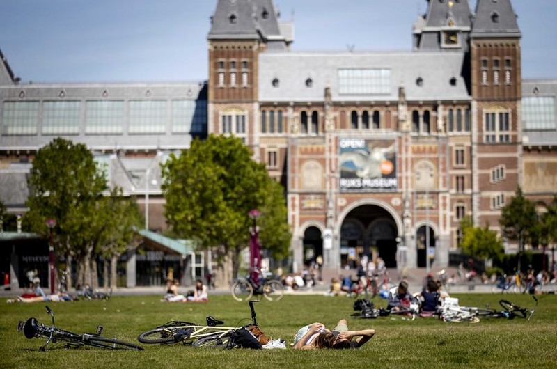 Olandezi care savurează vremea frumoasă, pe gazonul din fața Museumplein.