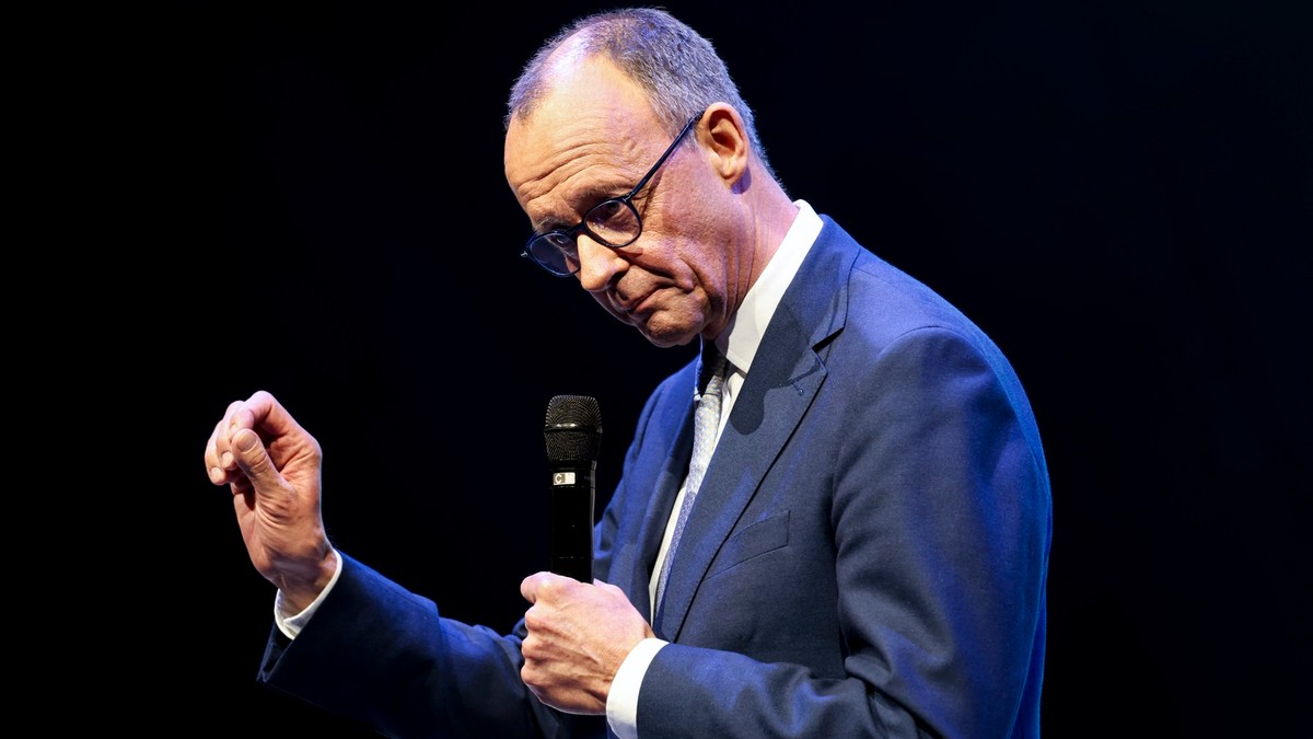 Friedrich Merz vorbește la microfon și este cu capul în jos, având un fundal negru în spate
