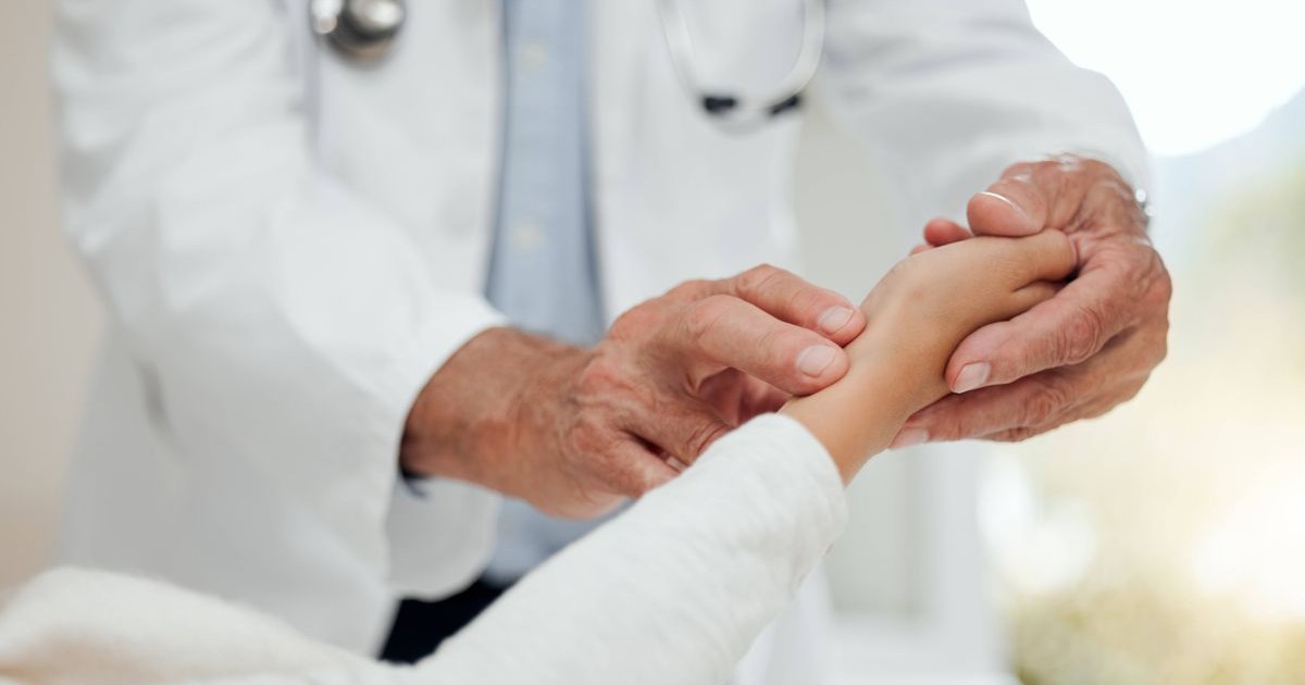 Un doctor ține mâna unui bolnav aflatîn pat pentru a-i lua pulsul