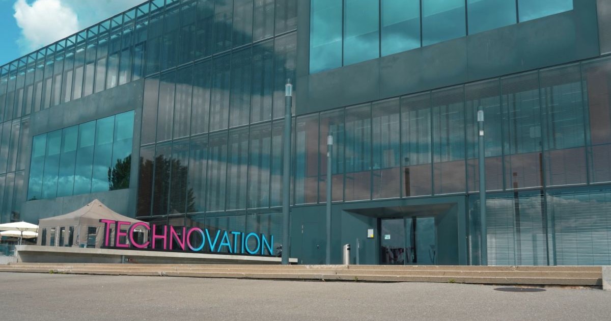 O clădire de sticlă din Neuchatel, Elvetia, în fața căreia e amplasat logo-ul conferinței Technovation, albatsru cu magenta, care aparține de Philip Morris International.