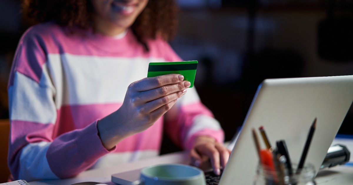 O femeie care ține cardul de la bancă în mână, în timp ce încearcă să plătească o factură pe laptop