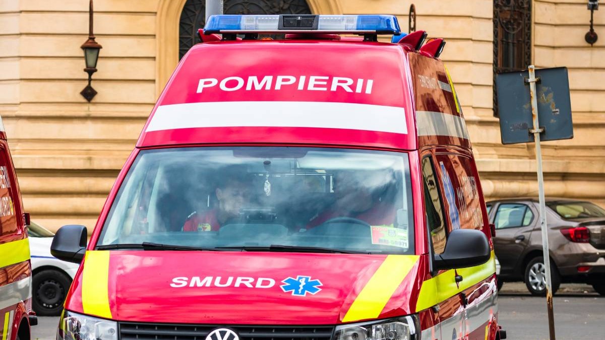 O ambulanță roșie SMURD parcată cu spatele, la volan și pe locul din dreapta al șoferului se află doi asistenți medicali care verifică niște acte