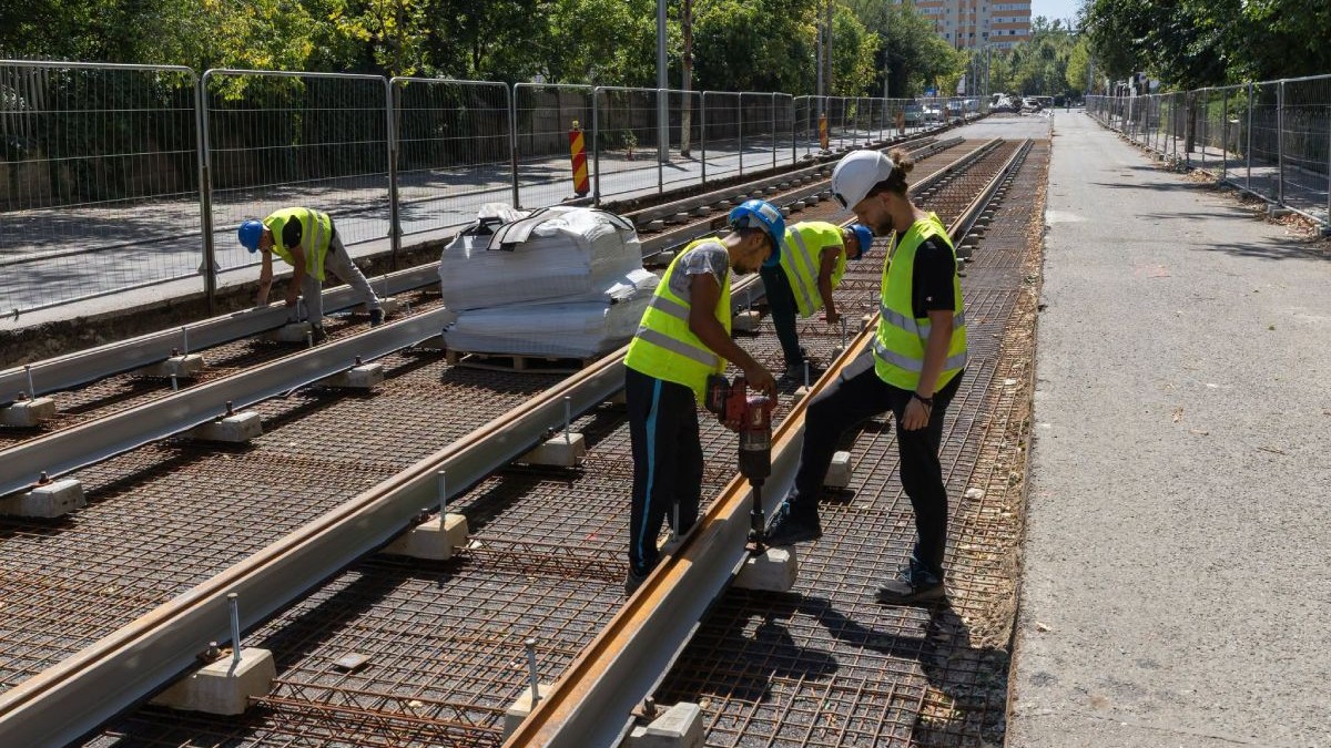 Muncitori îmbrăcați cu echipamente de protecție și căști pe cap, care lucrează la șinele de tramvai pe bulevardul 1 Decembrie 1918 din București, în august 2026