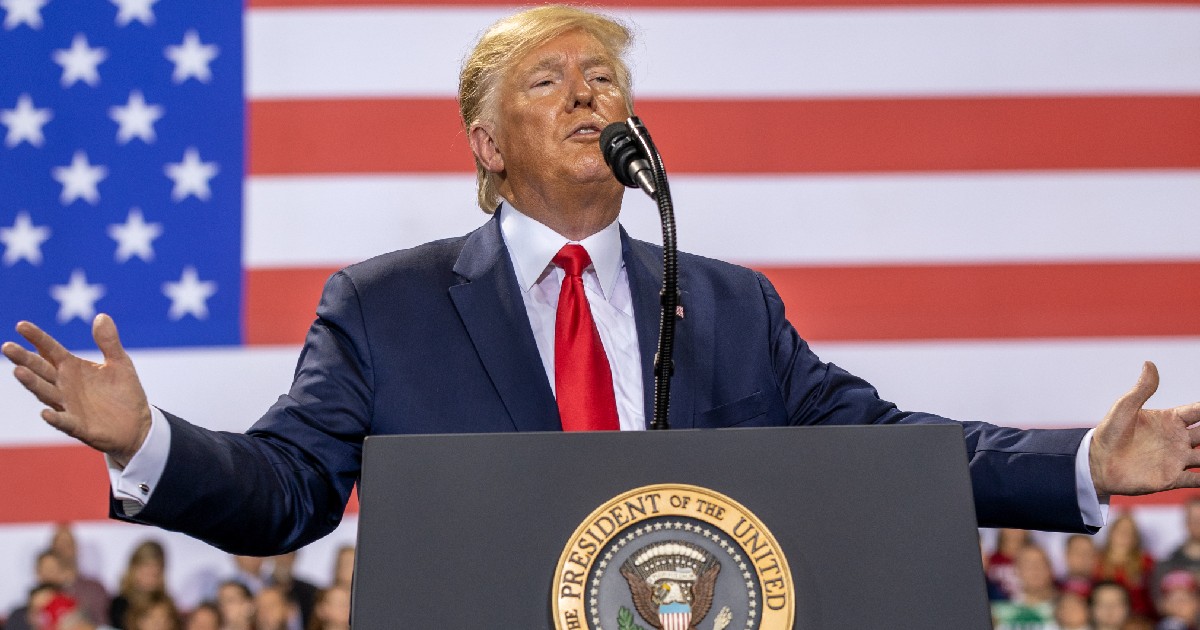 Imaginea îl înfățișează pe Donald Trump susținând un discurs de la o tribună oficială cu sigiliul prezidențial, având brațele desfăcute și steagul Statelor Unite ale Americii în fundal.