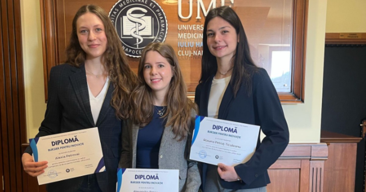 În imagine sunt ilustrate trei tinere care țin în mână diplome. Acestea sunt îmbrăcate formal, în ținută cu sacou