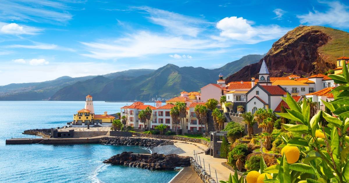 Vedere panoramică asupra satului Canical, lângă Ponta de Sao Lourenco. Insula Madeira, Portugalia, se vad case albe cu acoperiș portocaliu, apă limpede, munti in fundal si cerul albastru cu puțini nori