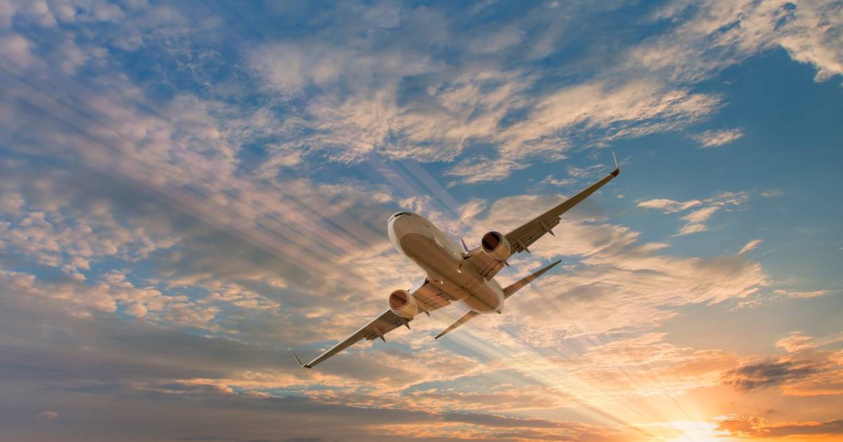 Avion zburând la apus, pe un cer albastru cu niste nori