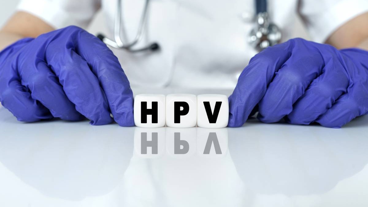 Vaccinarea anti-HPV prezentată de un medic în caginetul medical, doctorul poartă mânuși albastre și ține literele H,P și V pe masă