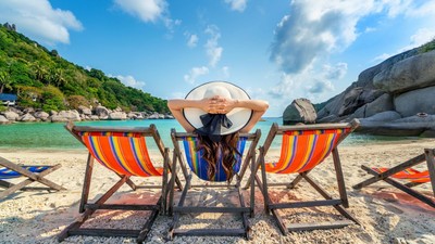Woman with hat sitting on chairs beach in beautiful tropical bea