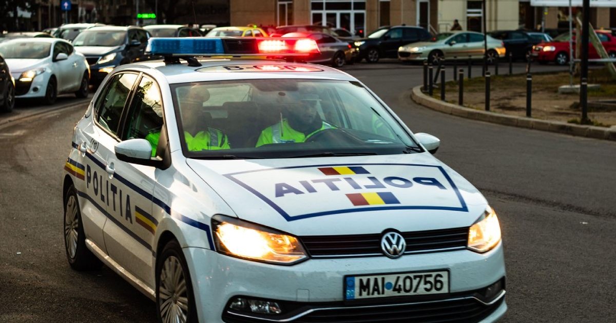 Mașină de Poliție Rutieră, cu girofarul pornit și farurile aprinse, pe o stradă
