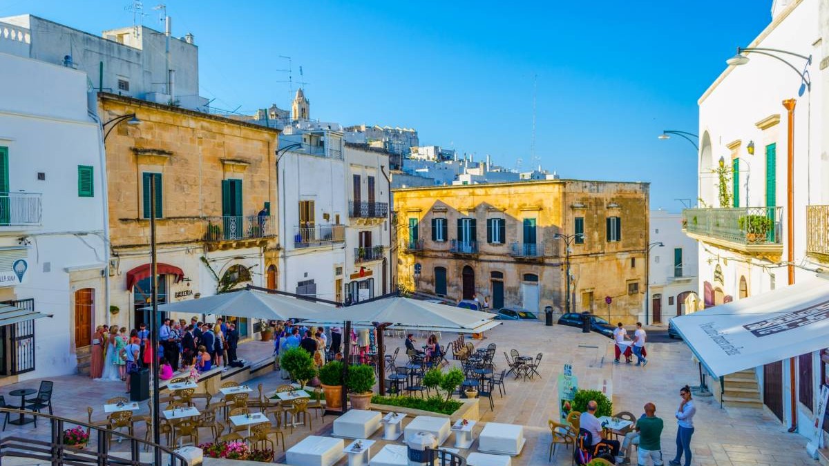 Două restaurante dintr-o piațtă din orașul Italian Ostuni, terasele au mesele goale, iar turiștii de îngrămădesc la magazinul de suveniruri de lângă