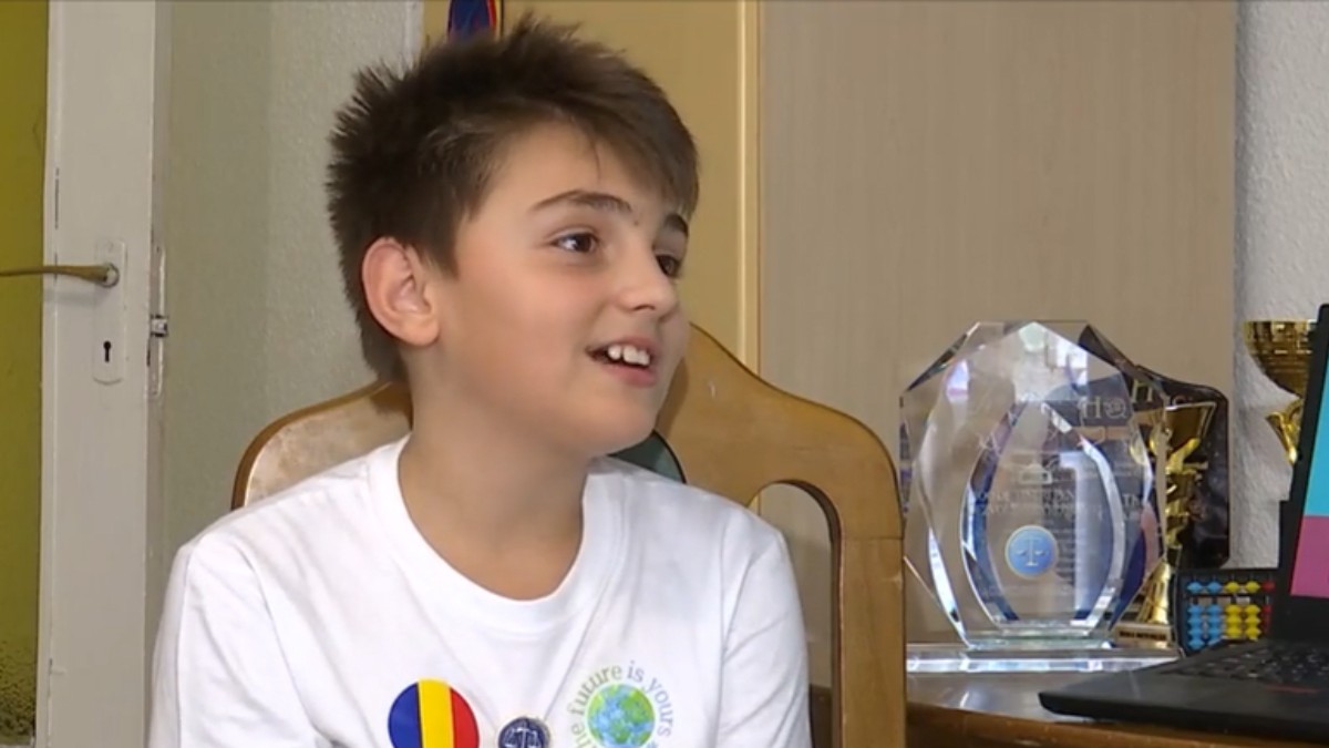 Karlos Tănăsucă îmbrăcat în tricou alb, în timp ce stă pe scaun și vorbește