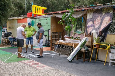 Câțiva bărbați din tabără montează în fața casei o umbrelă de soare
