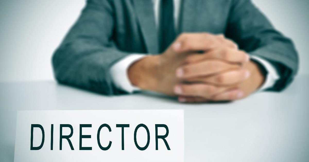 un bărbat în costum, așezat la un birou, cu o plăcuță cu numele în fața lui pe care scrie „director”