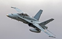 Un avion de luptă F/A-18 Hornet surprins în zbor în timp ce efectuează o manevră de urcare pe un cer înnorat.   