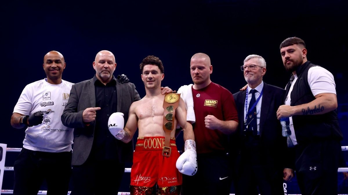 Fotografie de arhivă datată 251123 a boxerului irlandez John Cooney (centru), îmbrăcat într-o pereche de pantaloni scurți roșii cu o banderola pe care este scris numele său, alături de staff și antrenori