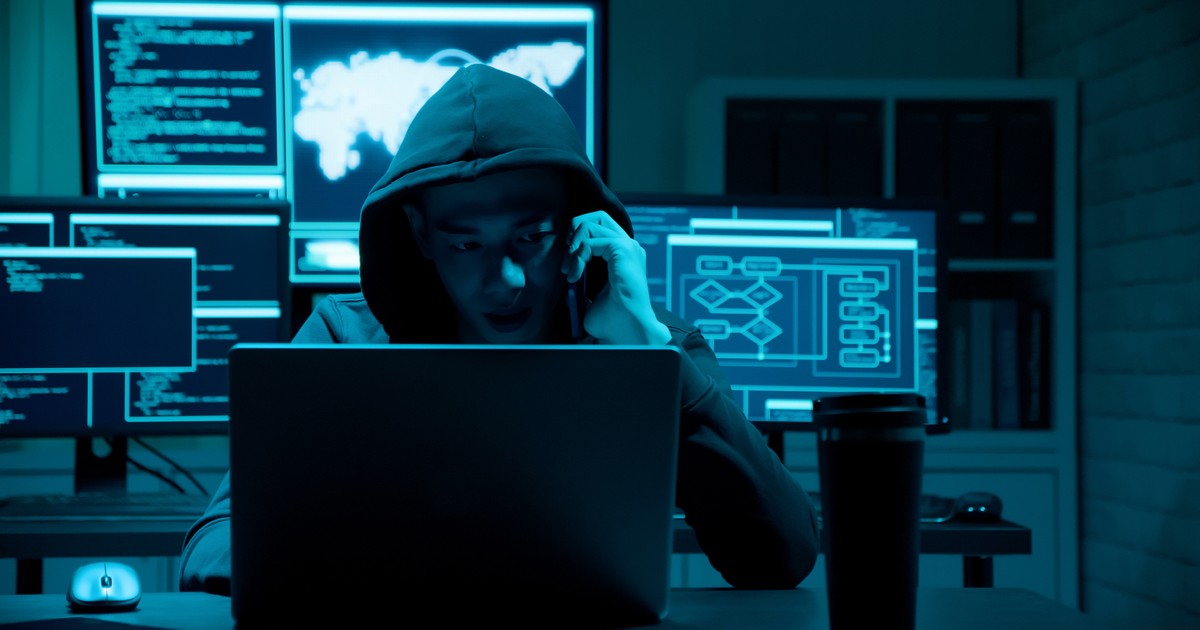 Infractor cibernetic cu hanorac, vorbind la telefon și înconjurat de calculatoare