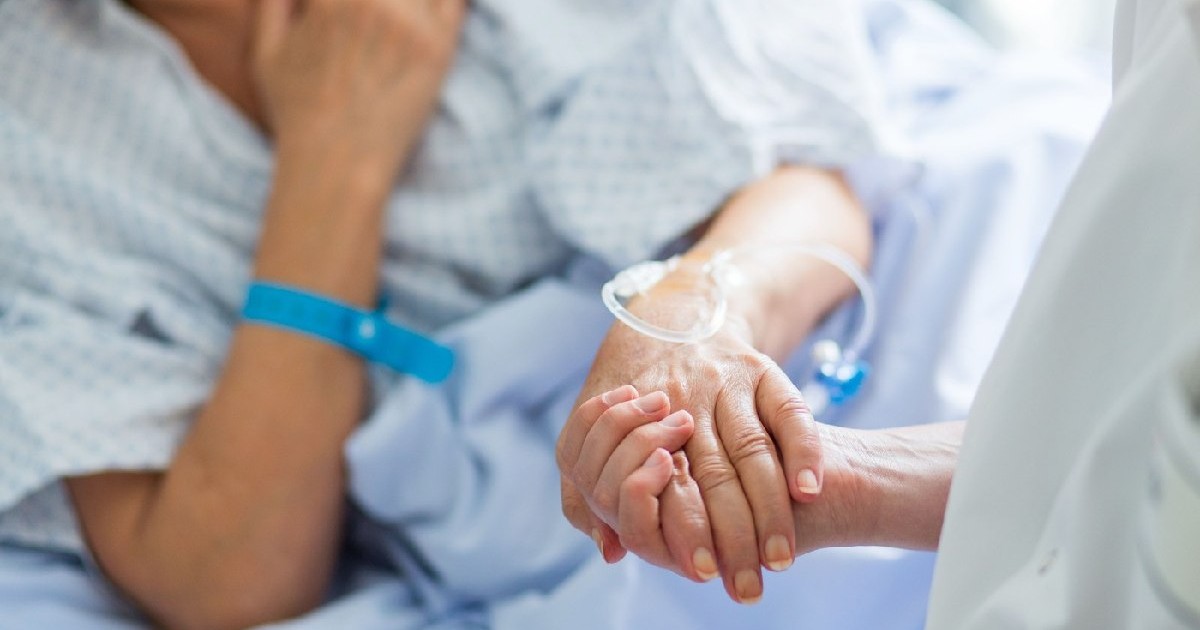 Un doctor ține de mână o femeie care stă într-un pat de spital