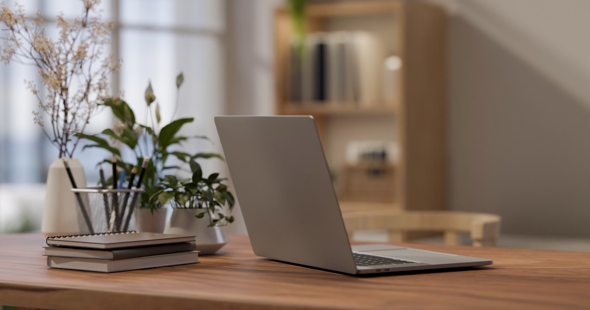 Un birou pe care sunt așezate un laptop, agende și plante.