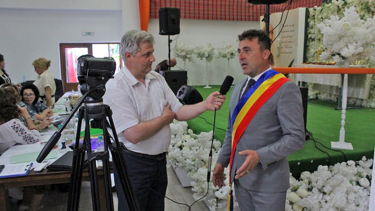 Un barbat grizonat in camasa alba ii ia un interviu unui primar in costum gri