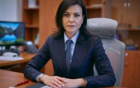 Cristina Chiriac în sacou albastru închis, cămașă albastră și cravată, în timp ce stă la birou