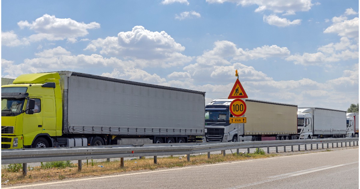 Mai multe camioane de diferite culori staționate în coloană, pe o autostradă