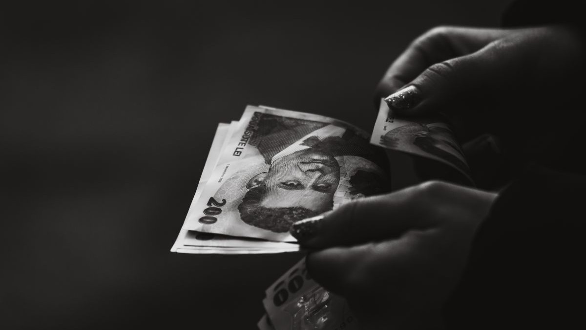 Mâna unei femei care numără bancnote românești de 200 de lei, pe un fundal negru