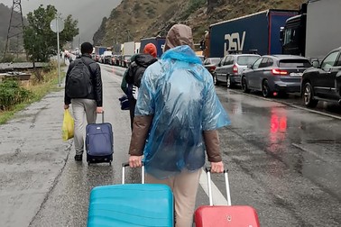 Oameni cu valize trec pe lângă vehicule cu numere de înmatriculare rusești pe partea rusă a frontierei spre punctul de control vamal Nijni Lars, între Georgia și Rusia, la aproximativ 25 km de orașul Vladikavkaz, la 25 septembrie 2022. Autoritățile ruse au recunoscut că există un aflux „semnificativ" de mașini care încearcă să treacă din Rusia în Georgia, la câteva zile după ce Moscova a anunțat o mobilizare parțială | Foto: Profimedia Images