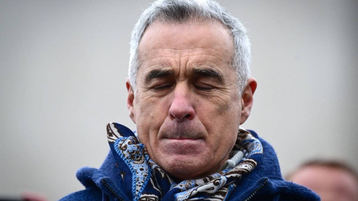 calin georgescu cu o figura incruntata purtand un pulover albastru si un fular la gat