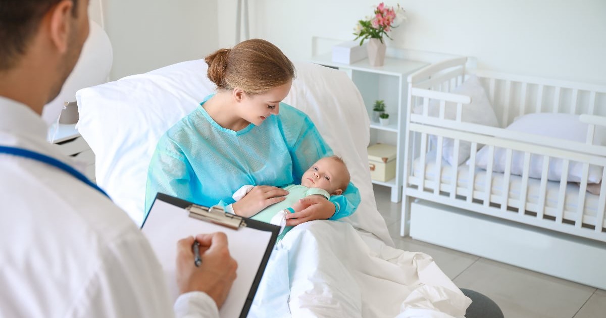 O mamă își ține în brațe nou-născutul într-un salon de maternitate, în timp ce un medic completează documentele medicale. Imaginea surprinde primele momente după naștere, într-un cadru care sugerează îngrijirea și monitorizarea stării de sănătate a mamei și copilului.